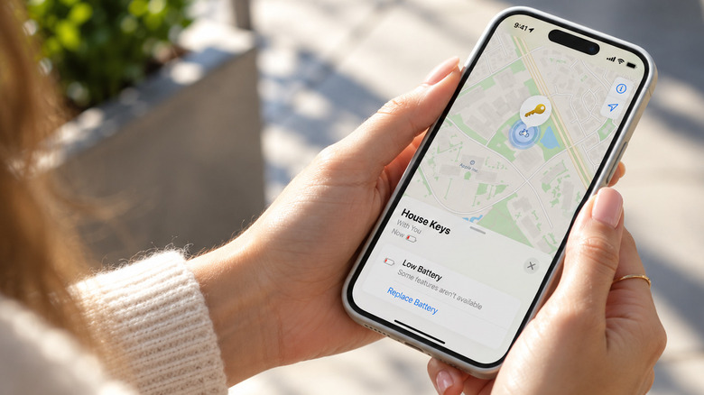 Hands holding an iPhone displaying a Low Battery warning for an AirTag named House Keys in Find My app.