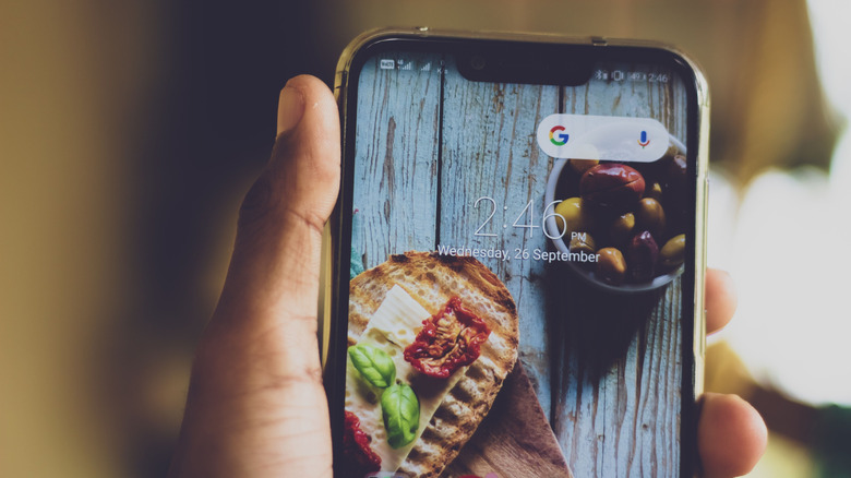 Hand holding Android phone with a wallpaper showing food