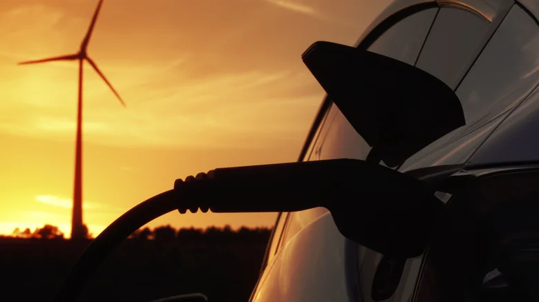 An EV charging at sunset, with the silhouette of a windmill in the background.