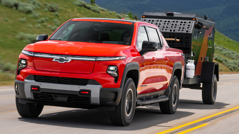 A red Chevy Silverado EV tows a packing trailer through a mountain landscape.