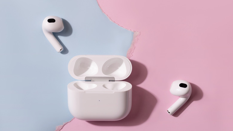 AirPods outside of their charging case on a blue and pink background.