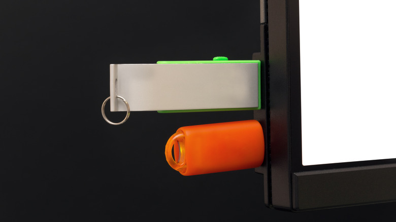 Two USB flash drives plugged into ports on the side of a computer monitor.