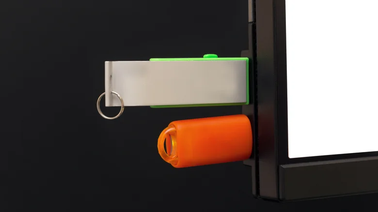 Two USB flash drives plugged into ports on the side of a computer monitor.