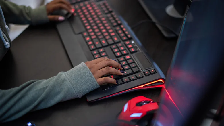 A person uses a backlit keyboard and mouse at a desktop computer setup.