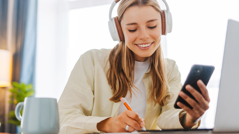 Woman wearing headphones while using phone and laptop