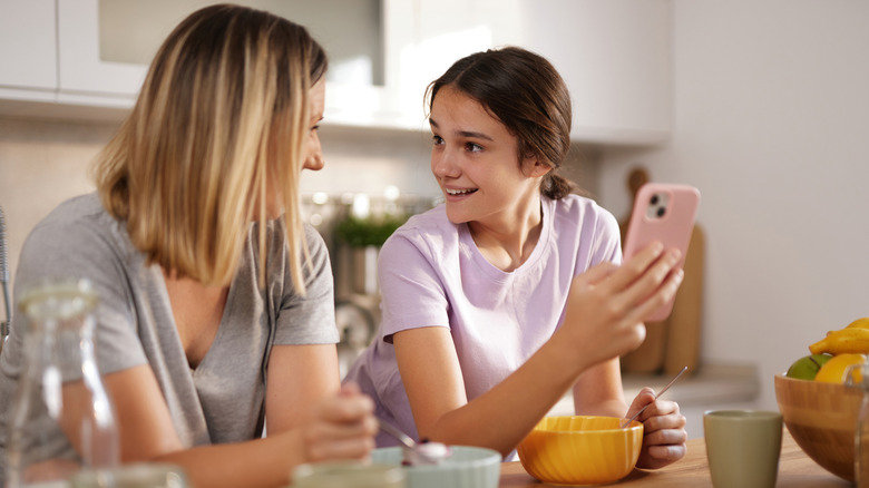 A mom and girl successful nan room smiling astatine 1 another, nan girl holding a phone.