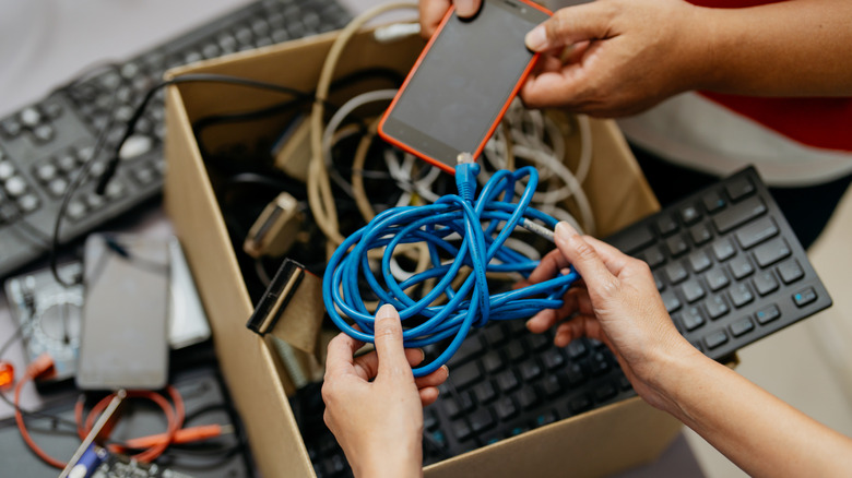 Hands onf group putting aged gadgets, including a phone, into a container for recycling.