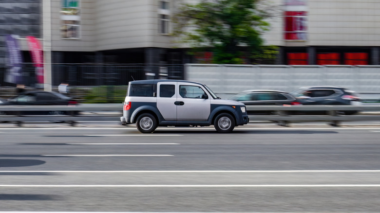 The Honda Element on a road with other cars blurry in the background.