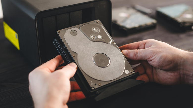 A man holding a hard drive in front of a home server.