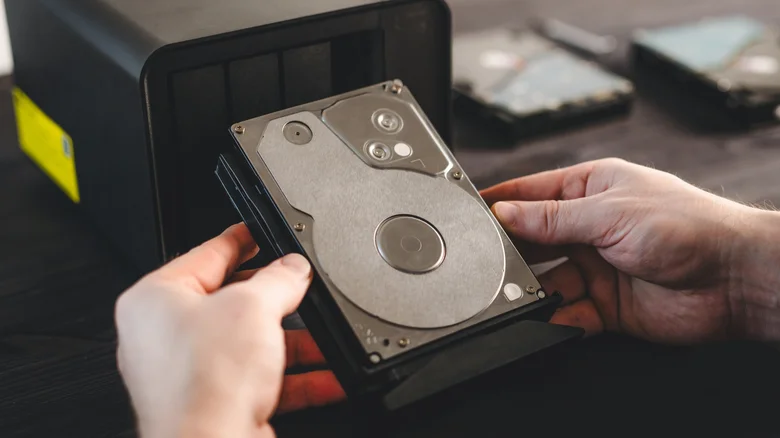 A man holding a hard drive in front of a home server.