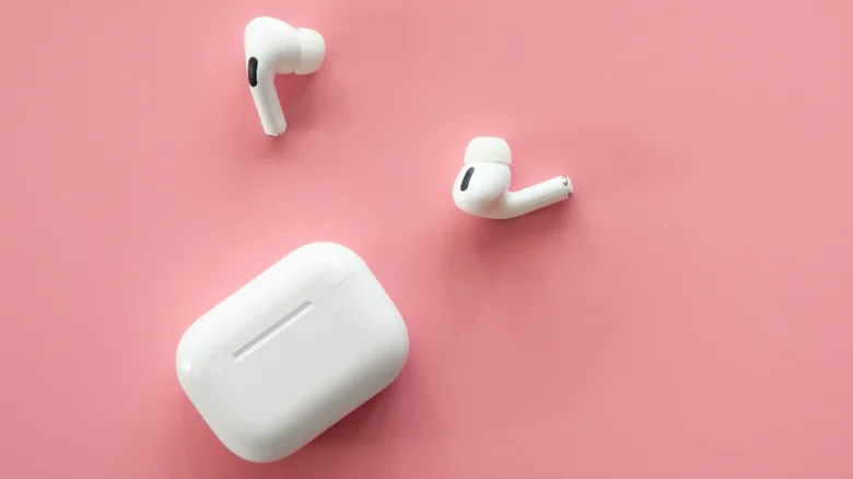 A pair of white earbuds and their case lay on a pink surface.