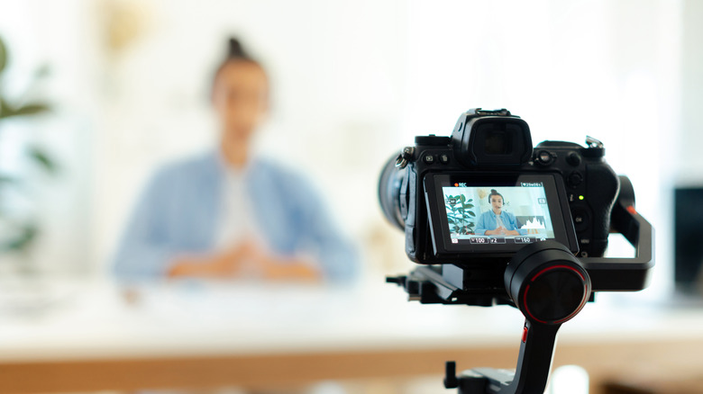 A blurred view of a person, with a digital camera prominently recording them