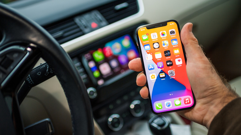 An iPhone being held, with a CarPlay display blurred in the background.