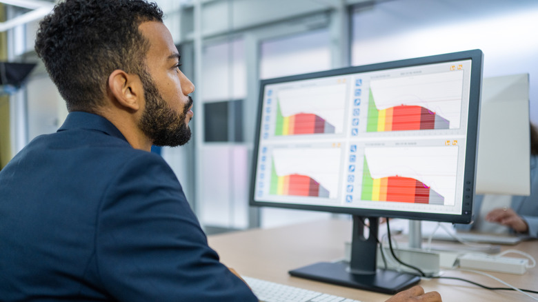 A man sitting at a computer looking at graphs on a monitor.