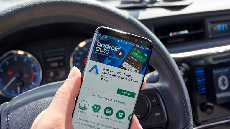 Person holding phone in car with the Android Auto app displayed.