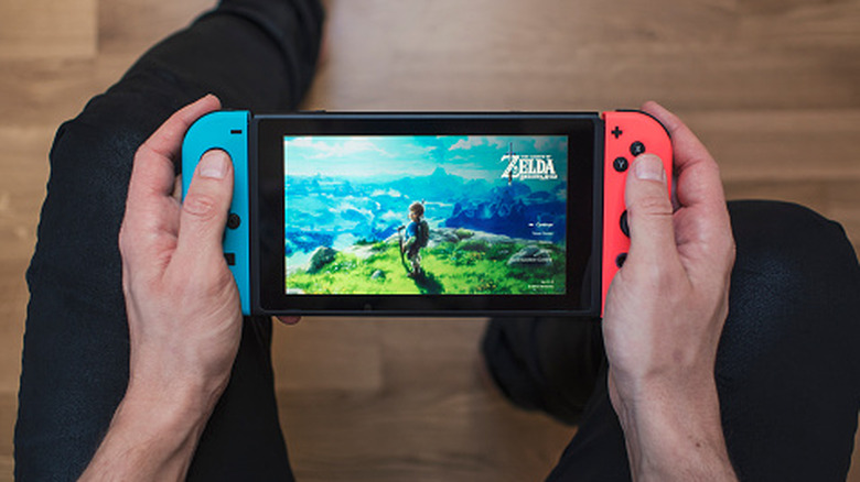 Person holding an original Nintendo Switch with blue and red Joy-Con controllers while playing "The Legend of Zelda: Breath of the Wild."