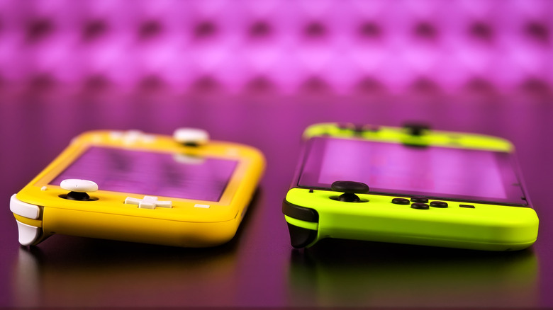 Yellow Switch Lite and green Nintendo Switch consoles resting side by side on a table.