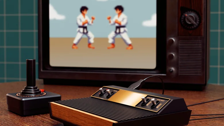 An Atari 2600 video game console and controller with a karate game on an old TV in the background.