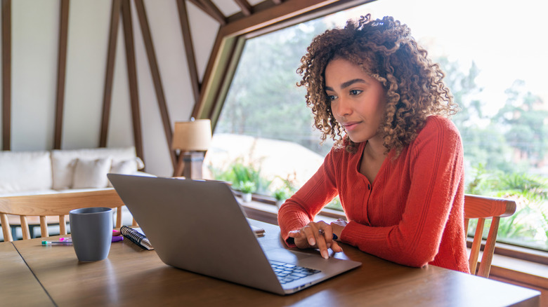 A woman working on a laptop with a window behind her