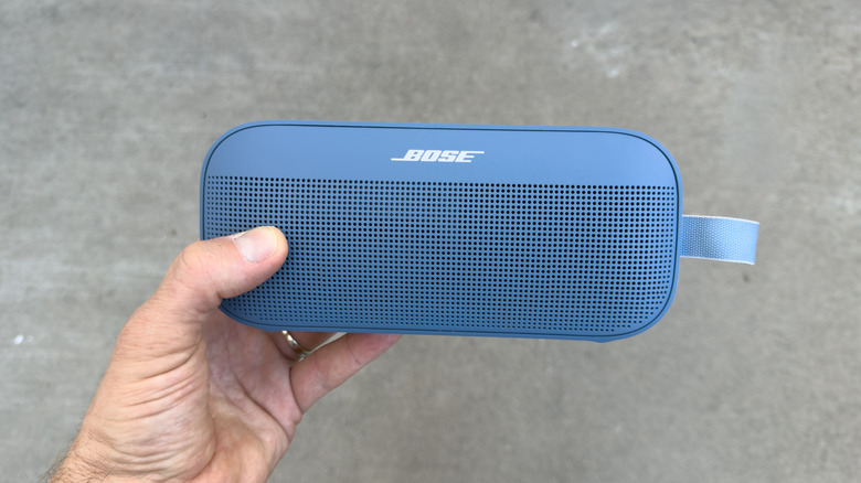 Bose Bluetooth speaker held against grey background.