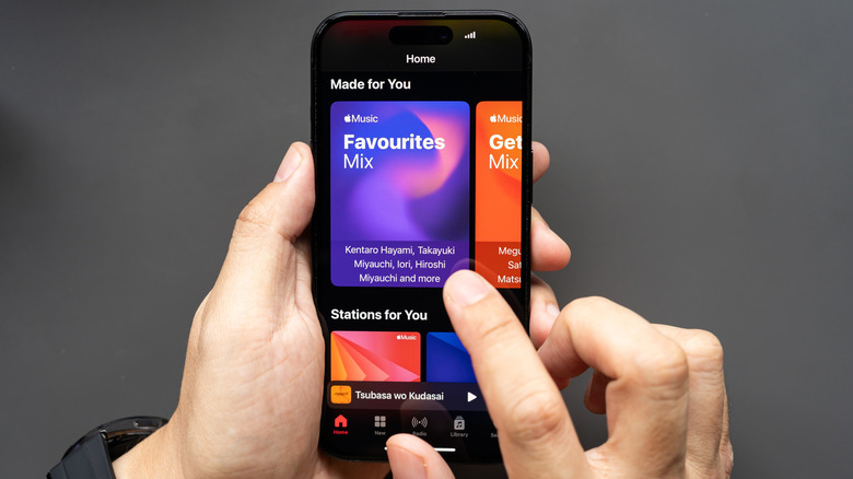 Hands holding an iPhone showing Apple Music, with the Home screen showing personalized mixes and stations.