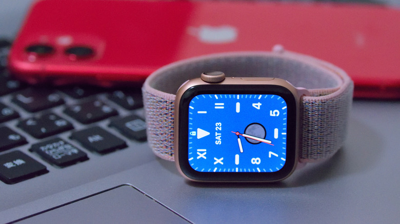 An Apple Watch with a blue California watch face and a Sport Loop, in front of a red iPhone.