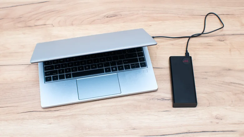 Half-closed laptop charging from a connected portable power bank.