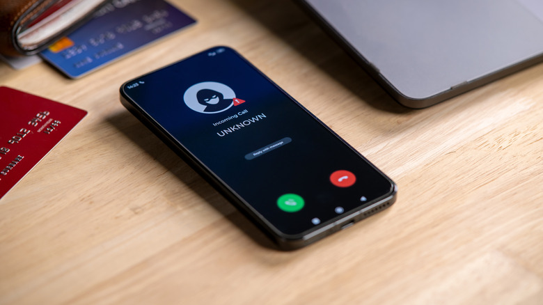 A black phone on a wooden desk receiving a call from an unknown caller.