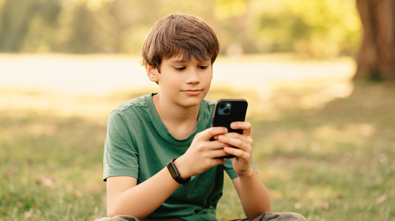 A young boy using an iPhone while sitting outside.