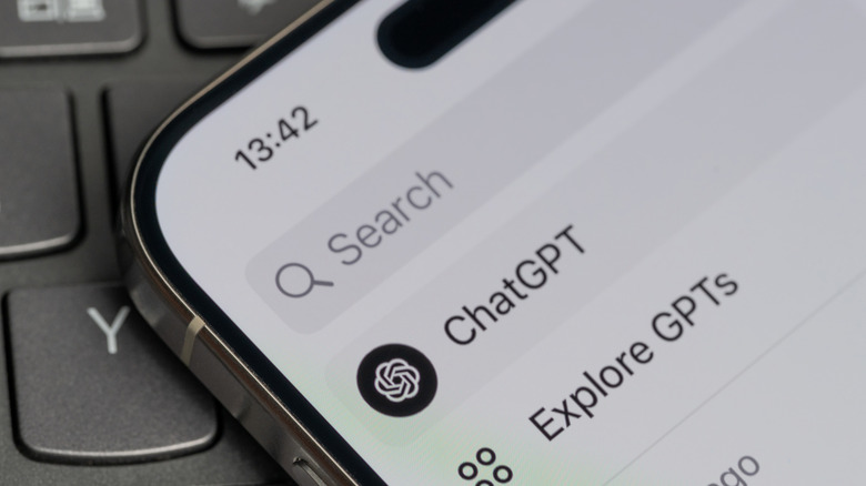 Close-up of a smartphone displaying ChatGPT in a search interface while resting on a computer keyboard.