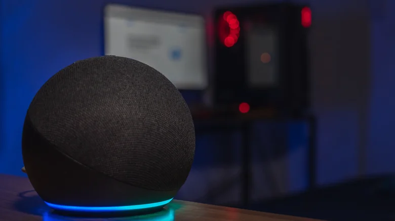 Dark room picture of an Amazon Echo, a blurry computer screen and tower in the background.