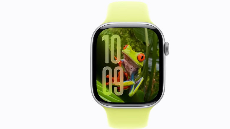 An Apple Watch with a bright green strap shows a colorful frog climbing a leaf as its watch face.