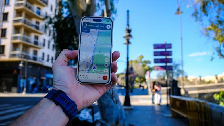 A hand holding up a smartphone using Google Maps in a city.