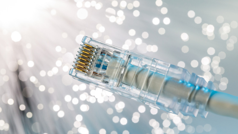 A transparent RJ45 connector attached to a light-colored Ethernet cable against a blurred, sparkly background.