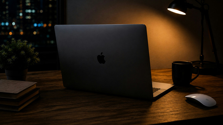 Dimly lit view of a MacBook (view from behind) on a desk
