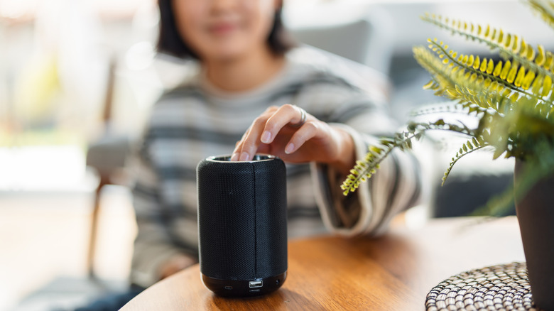 Woman adjusting volume on Bluetooth speaker.