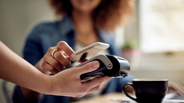 A woman at a cafe holding her phone over a contactless terminal to pay.
