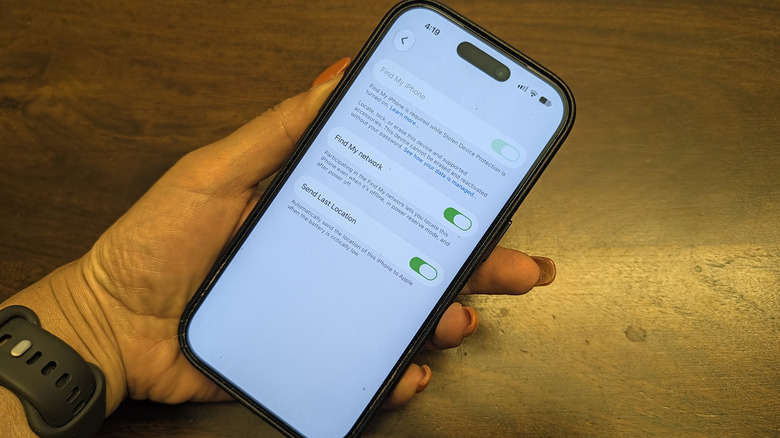 A hand holding an iPhone, showing the Apple Find My network options.