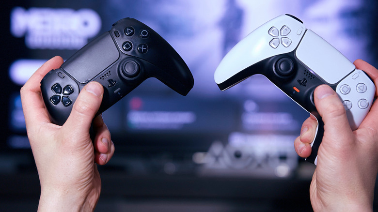 A person holding up two PS5 controllers, one black and one white.