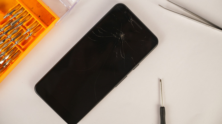 An iPhone with a cracked screen lying on a table.