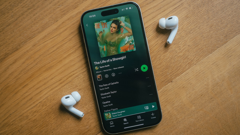 An iPhone with two AirPods showing Taylor Swift's "The Life of a Showgirl" album on Spotify.