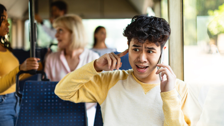 Young man taking a phone call in a crowded and noisy bus.