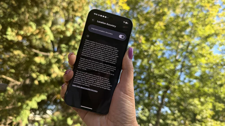 A hand holding a Google Pixel 11 Pro showing the Location Accuracy setting.