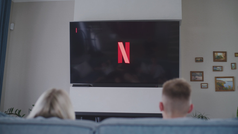 Netflix logo displayed on TV, two people watching on the couch.