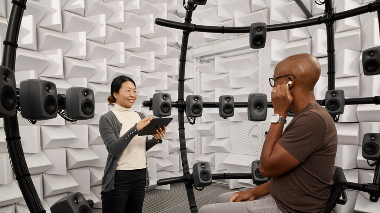 A woman and a man in Apple's audio testing labs testing AirPods, surrounded by speakers.
