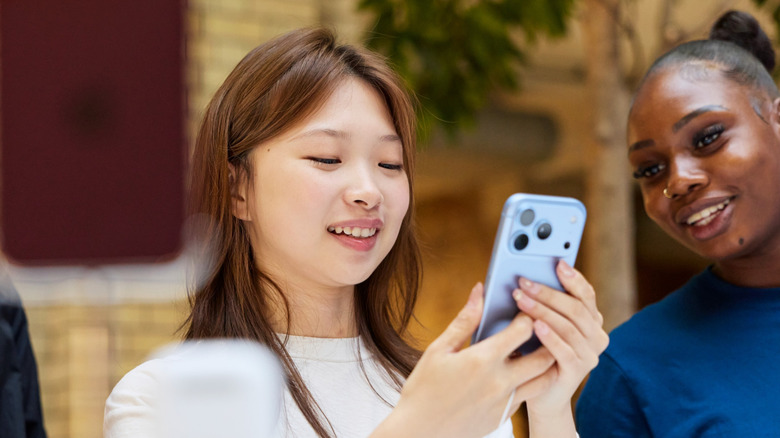 A woman holding a blue iPhone with another woman looking at it.