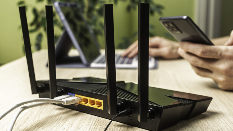Hand holding smartphone near a wireless router with cables connected.