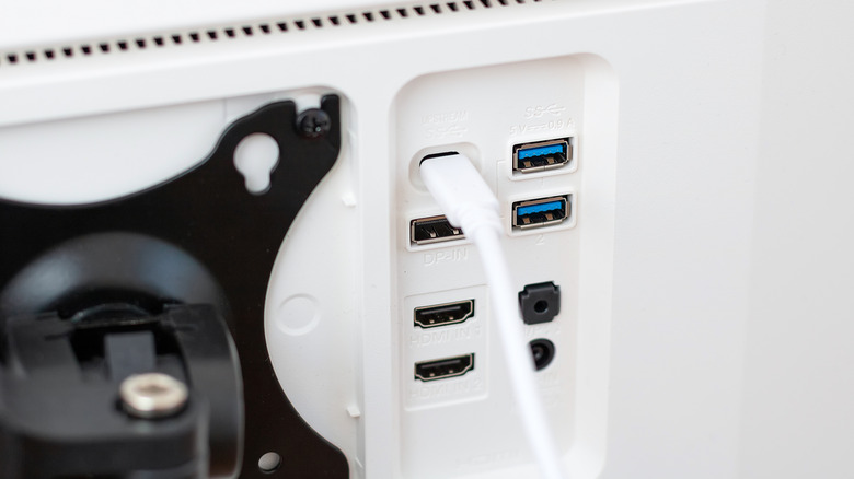 A USB-C cable plugged into the back of a computer display, showing various other ports.