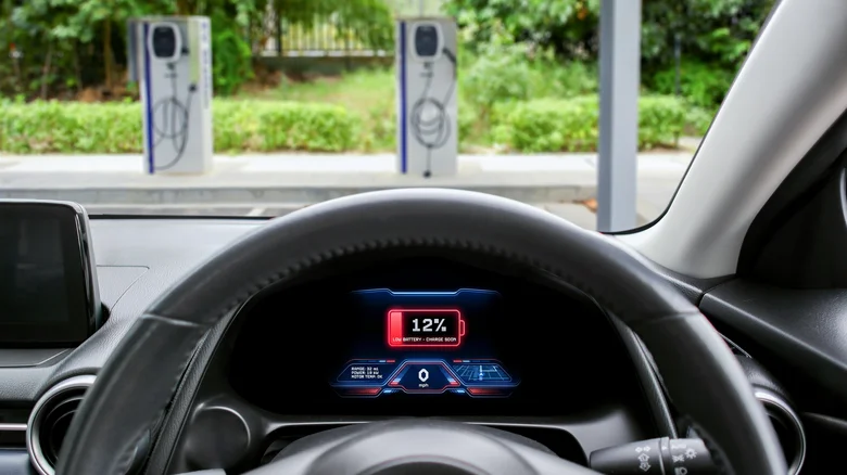 View from inside an electric vehicle showing a low-battery warning at 12 percent with charging stations visible ahead.
