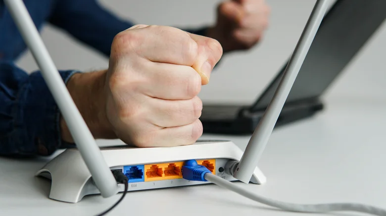A human fist, placed on top of a Wi-Fi router, with a laptop blurred in the background.
